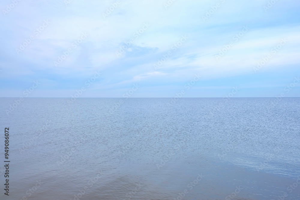 Fototapeta premium Ein weiter Blick auf das Meer unter einem blauen, bewölkten Himmel vermittelt Minimalismus und Einsamkeit
