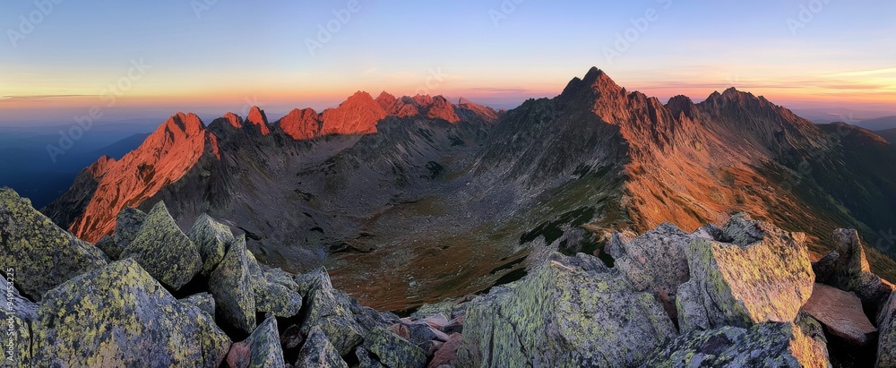 Obraz premium Panoramic view of the Tatra Mountains at sunset, showcasing rugged peaks, craggy cliffs, and dramatic rocky terrain.