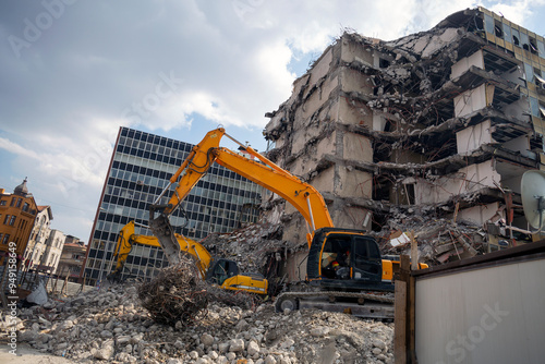 Excavators work amidst rubble, demolishing a partially collapsed building in an urban area.