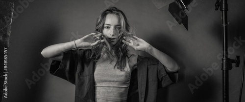 A black and white artistic portrait of a woman posing with an expressive look in a studio environment, highlighting emotion and contemporary fashion style.