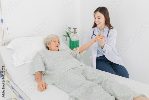 Asian female doctor comforting elderly patient in hospital bed, holding hands with compassion. Medical care and support for senior woman. Doctor assessment symptoms and plan to rehabilitation.