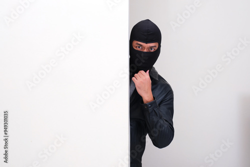 A thief wearing balaclava peeking from behind wall photo