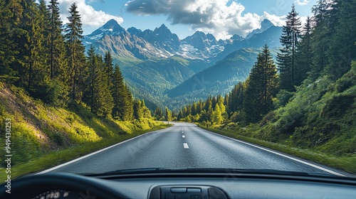 1. A peaceful view from inside the car shows a winding mountain road with lush green trees lining the path, while the distant peaks are capped with snow under a bright blue sky. The dashboard is in photo