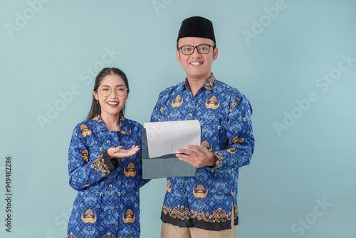 Two Indonesian government workers in blue batik uniform holding a document, discussing about task. photo