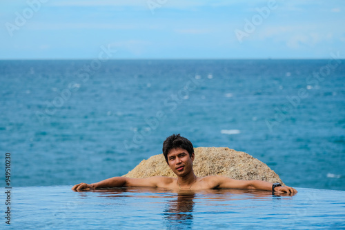 A man relaxing in a swimming pool at a luxury resort with blue sky and blue sea background. Young man enjoying beautiful sunset in luxury hotel near swimming pool. Calmness and serenity.