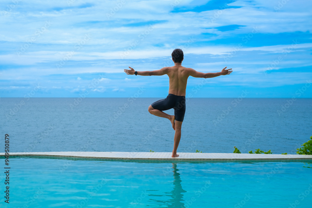 Fototapeta premium Man doing yoga and meditating in tree position near swimming pool on the tropical beach in Samui, Thailand. Healthy lifestyle active balanced practicing meditate and energy, yoga in morning.