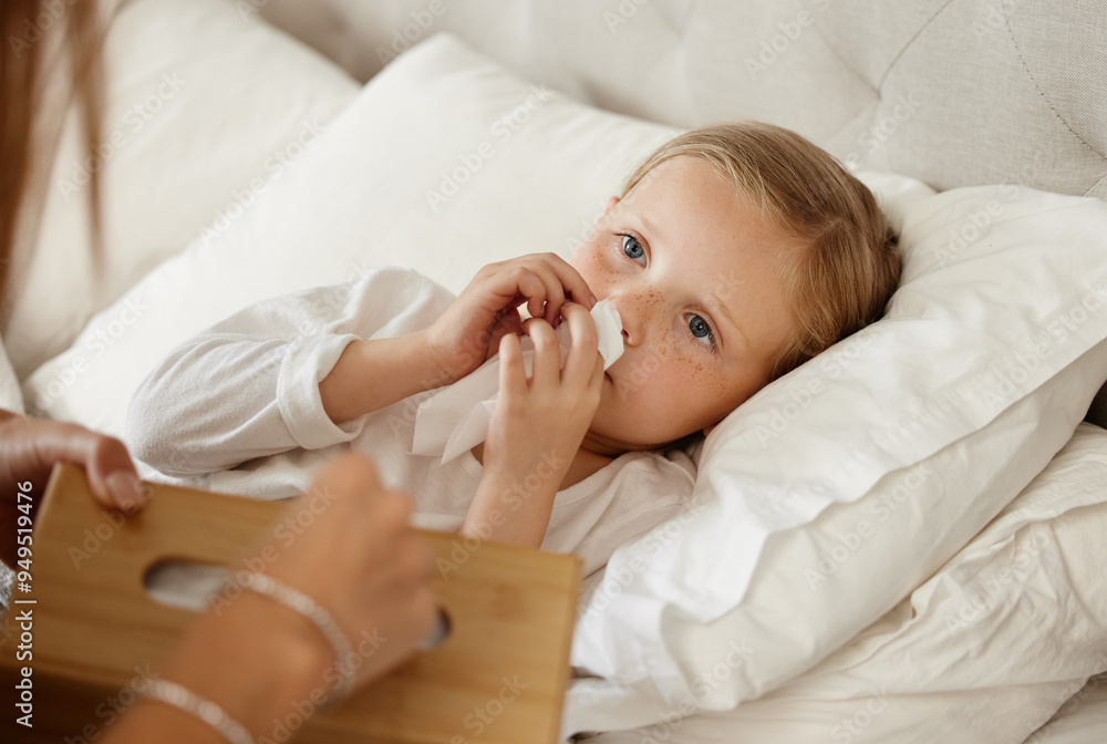 Sick, child and parent at bed in home for healthcare, wellness or tissue for cold treatment. Health, person and girl blowing nose for flu, virus or infection in bedroom with care, comfort and support Sick, child and parent at bed in home for healthcare, wellness or tissue for cold treatment. Health, person and girl blowing nose for flu, virus or infection in bedroom with care, comfort and support