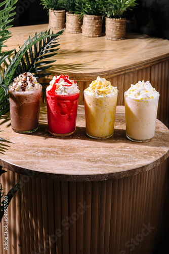 Four colorful milkshakes topped with whipped cream sitting on a stone table