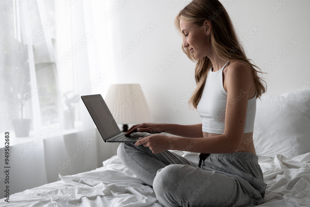 Naklejka premium woman sitting on bed in bedroom, working on her laptop in the morning