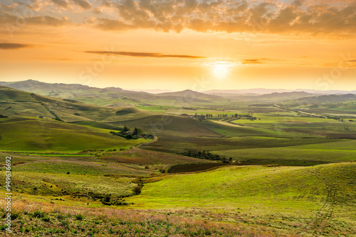 spring season green landscape of green field and meadow in a hill countryside with mountains and beautiful sunset sky on background