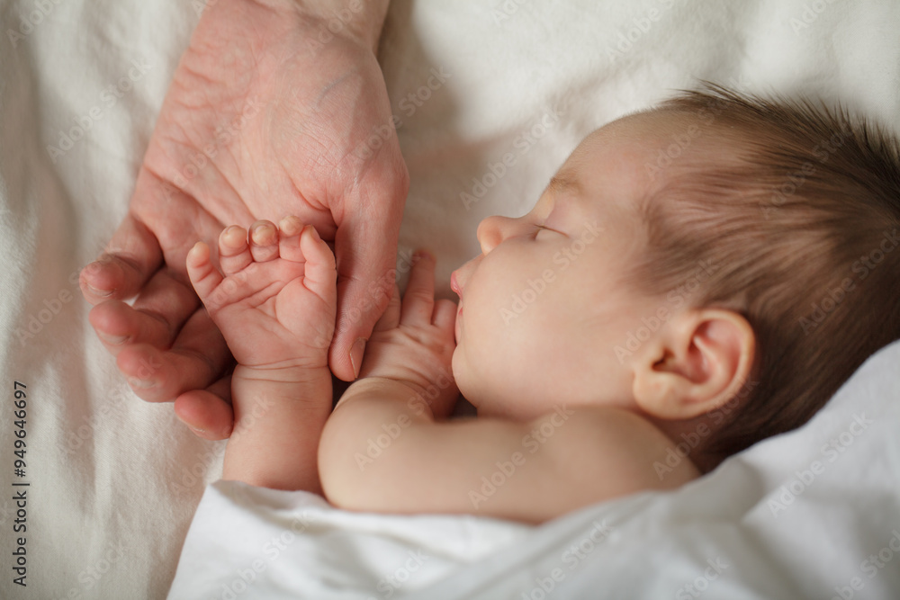 Little Baby's hand into parent hands. Family happiness concept. Sleeping newborn in first days of life at home. Father holding baby hand. Little Baby's hand into parent hands. Family happiness concept. Sleeping newborn in first days of life at home. Father holding baby hand.
