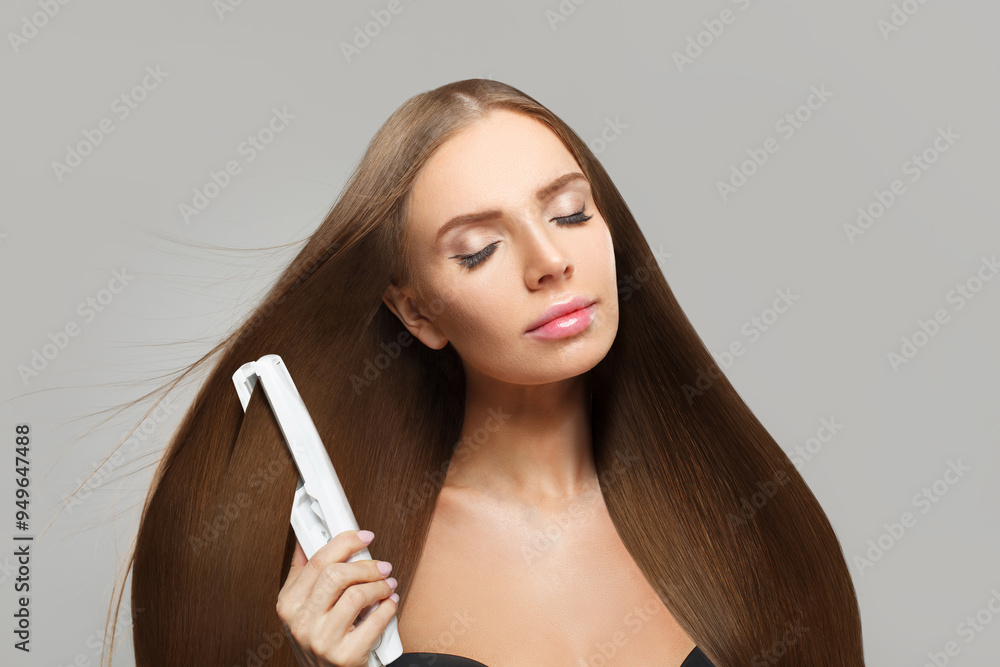 Obraz premium Pretty brunette woman holding straight hair iron and straightening her long smooth shiny hair on white background. Haircare, hairstyle, hairdressing and hair styling concept