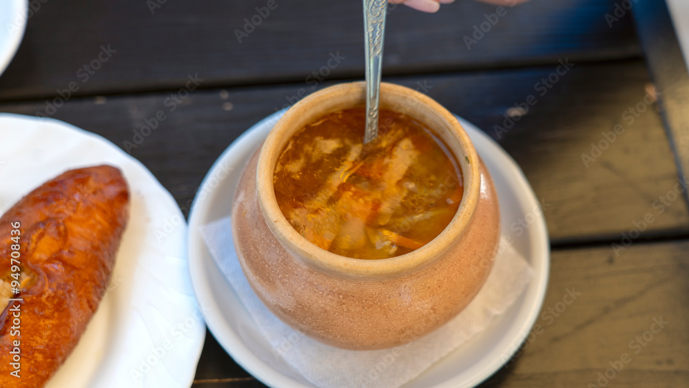 A person is eating soup from a large bowl. The bowl is on a white plate and is filled with a thick, brown soup. A spoon is being used to eat the soup A person is eating soup from a large bowl. The bowl is on a white plate and is filled with a thick, brown soup. A spoon is being used to eat the soup