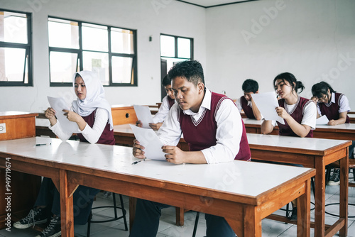 Multiethnic Asian Students In Uniform Sitting In Classroom Doing An Exam 