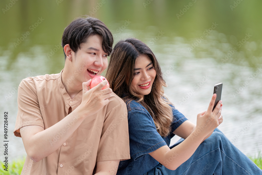 Asian couple sharing joyful selfie moment during lakeside picnic