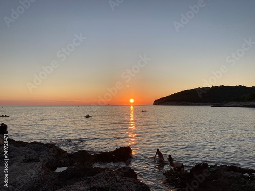Sunset in Croatia, Pula. Amazing view of the orange sunset with blue sky and clouds on the sea and some trees in the forest in the background with rocky beach. 