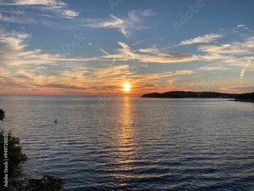 Sunset in Croatia, Pula. Amazing view of the orange sunset with blue sky and clouds on the sea and some trees in the forest in the background with rocky beach. 