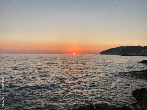 Sunset in Croatia, Pula. Amazing view of the orange sunset with blue sky and clouds on the sea and some trees in the forest in the background with rocky beach. 