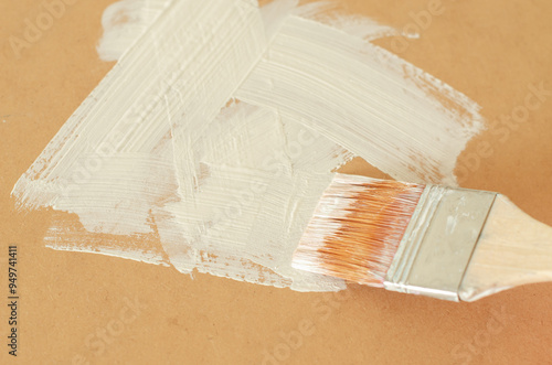A paintbrush painting a surface with white paint.
