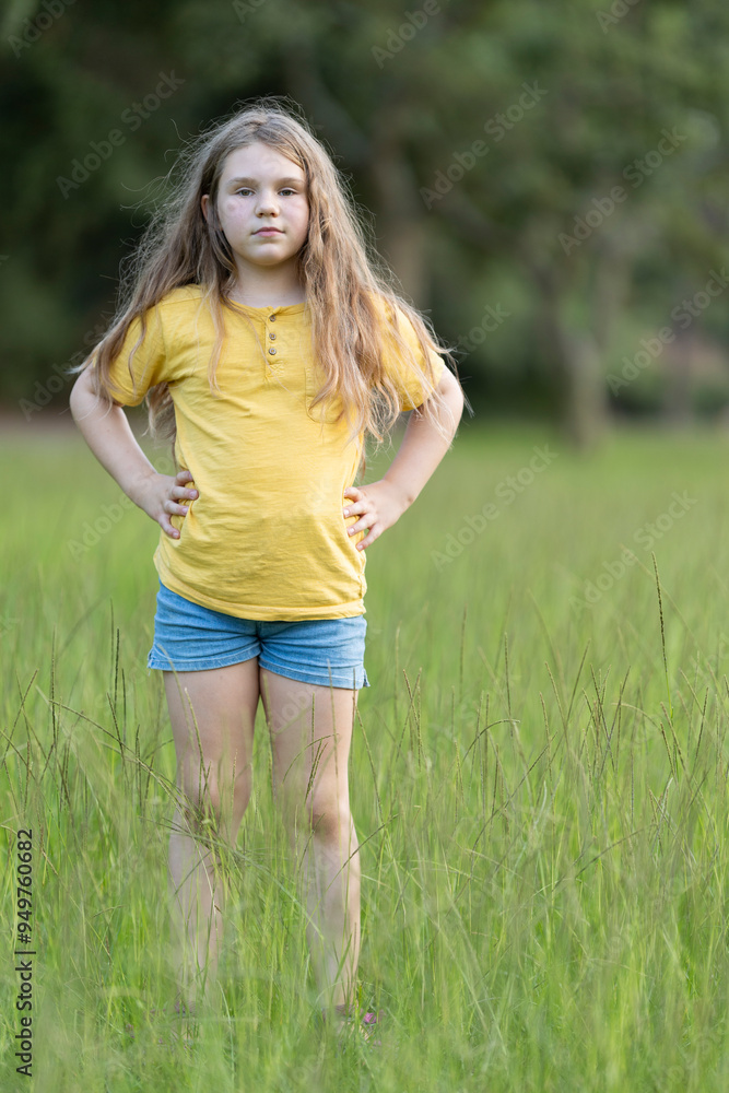 Young girl standing with hands on hips in tall grass field Young girl standing with hands on hips in tall grass field