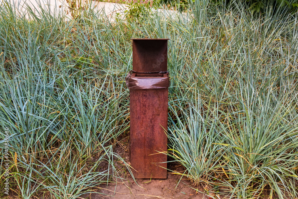 Obraz premium Square metal trash can. Rectangular rusty trash can stands on the ground outdoors