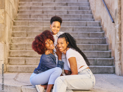 two young women sit on a staircase, smiling and hugging each other. Scene is warm and friendly