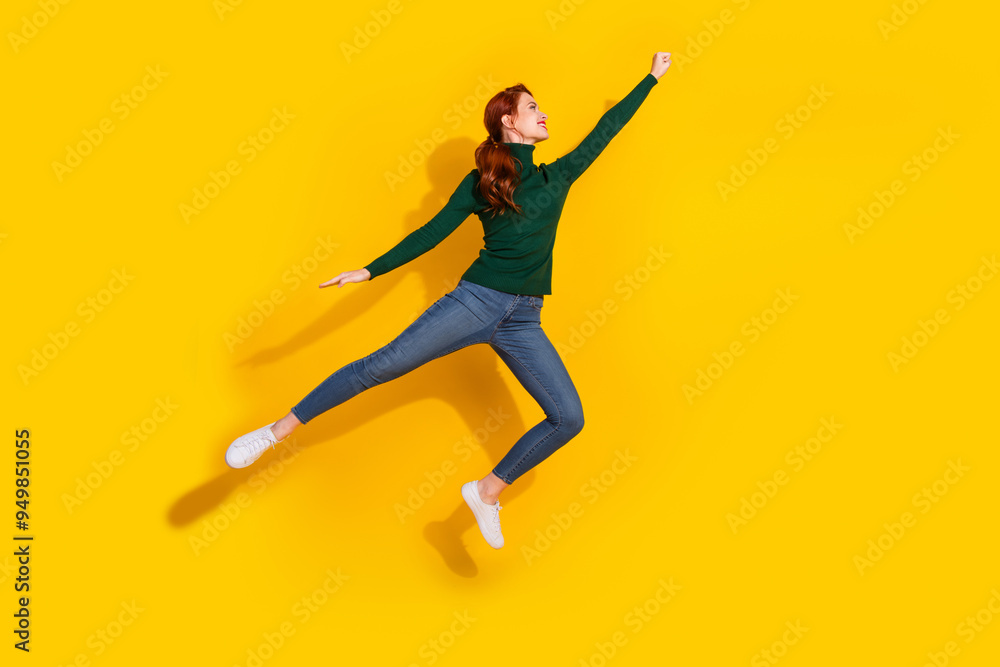 Full length photo of shiny attractive lady dressed green sweater jumping hign rising fist empty space isolated yellow color background Full length photo of shiny attractive lady dressed green sweater jumping hign rising fist empty space isolated yellow color background