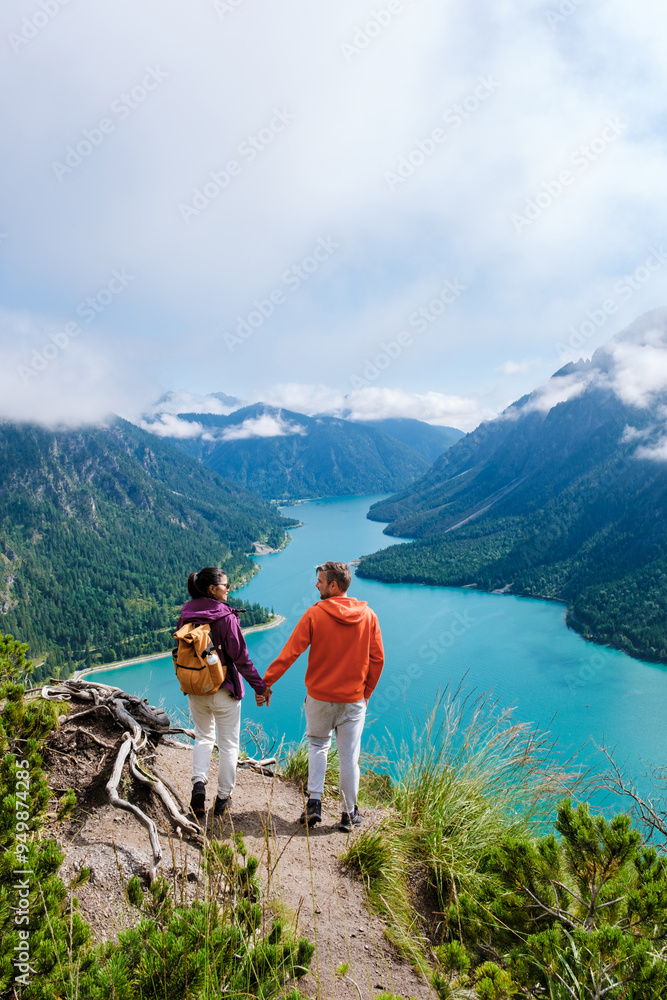 Obraz premium Two hikers enjoy breathtaking views over the turquoise lake in Plansee, Austria on a clear day