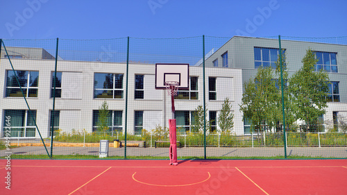 Schoolyard with basketball court and school building exterior in the sunny day. 