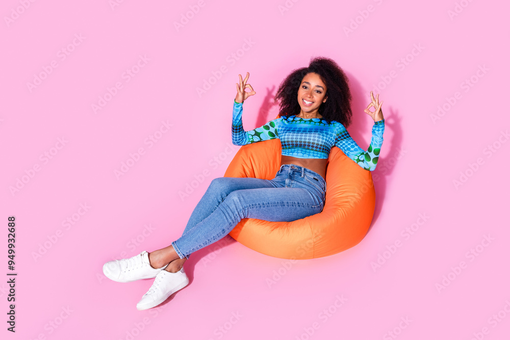 Full body photo of attractive young woman sit orange beanbag show okey dressed stylish blue clothes isolated on pink color background Full body photo of attractive young woman sit orange beanbag show okey dressed stylish blue clothes isolated on pink color background