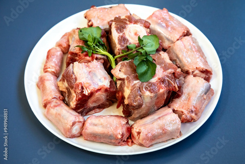 Raw beef oxtail on a round white plate in closeup.