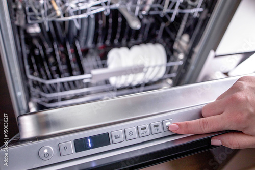 Woman's hand turns on the dishwasher to wash the dishes. Built-in appliances in the kitchen. photo