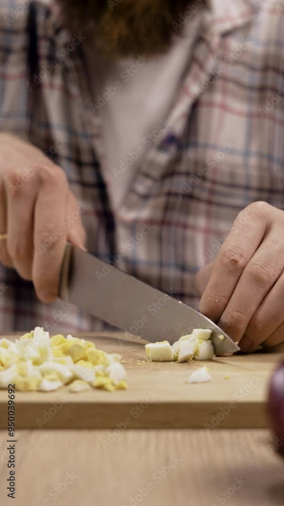 Man preparing salad in kitchen chopping boiled eggs cutting egg with knife on wooden chopping board, home cooking concept Man preparing salad in kitchen chopping boiled eggs cutting egg with knife on wooden chopping board, home cooking concept