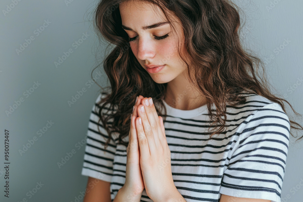 Side view of woman wearing striped T-shirt holding hands in prayer and asking for help.