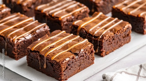 Decadent homemade salted caramel brownies with a glossy caramel drizzle topping served on a white platter for a tempting dessert or party presentation