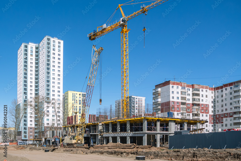 A construction site where tower and crawler cranes perform lifting work. A new house is being built on the site of the old houses. A road is being paved near the house under construction. A construction site where tower and crawler cranes perform lifting work. A new house is being built on the site of the old houses. A road is being paved near the house under construction.