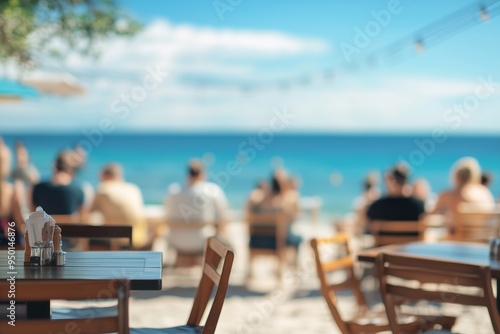 Blurred people sitting at tables in an outdoor beach cafe, with the seashore and sea in the background. Concept of relaxed seaside dining and social gatherings.