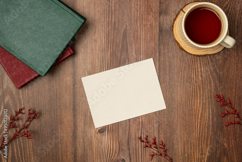 Mockup in vintage style with empty white paper list, books, cup of tea on wooden background from above. Space for text