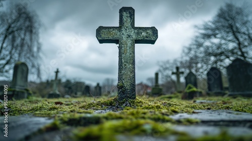 Close-up of a mossy concrete cross seen from a low angle, standing solitary in an old, neglected cemetery under a moody sky.