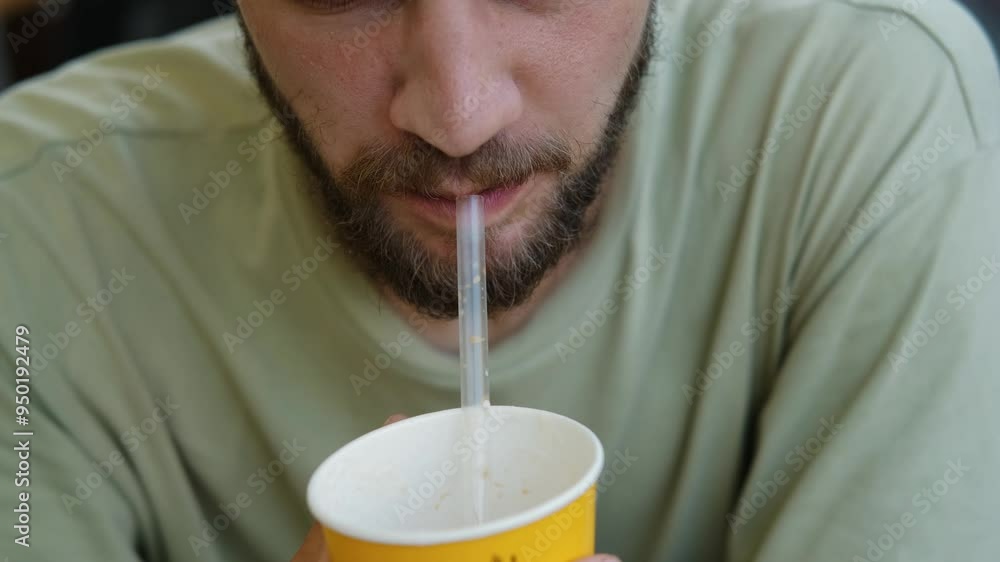 Coffee time at cafe. A young handsome Caucasian man is sitting on terrace and drinking hot coffee from paper cup using a straw. Enjoying the peace of good morning Coffee time at cafe. A young handsome Caucasian man is sitting on terrace and drinking hot coffee from paper cup using a straw. Enjoying the peace of good morning