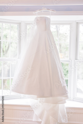 A wedding dress hung up against a window 