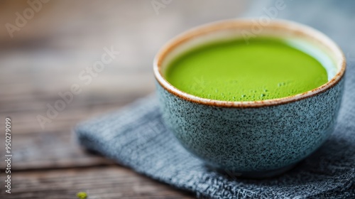 A beautifully crafted ceramic cup filled with vibrant green matcha tea, placed on a textured grey cloth, representing elegance and traditional tea culture.