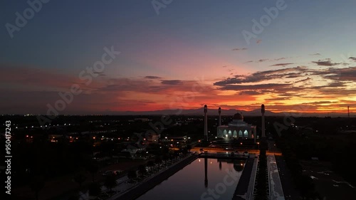 Mosque at Sunset: A breathtaking aerial view of a mosque silhouetted against a vibrant sunset sky, its reflection shimmering in a tranquil pond. The scene evokes a sense of peace and serenity, capturi