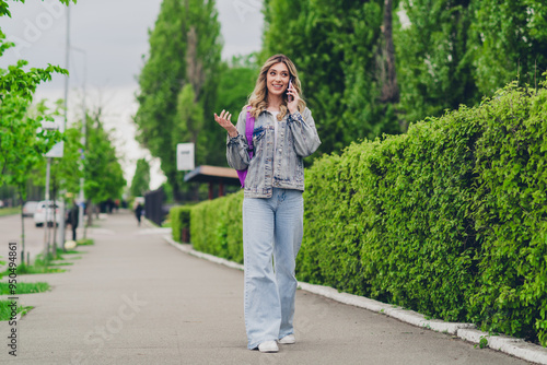 Full size photo of nice young woman speak phone backpack wear denim jacket walk city center outdoors