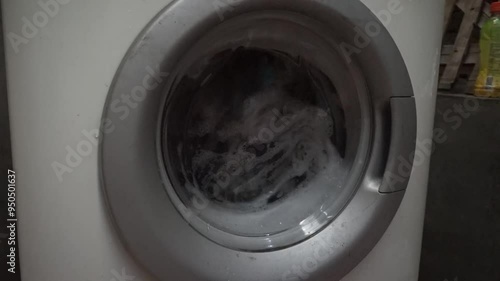 Closeup of a washing machine door with clothes and soapy water inside.