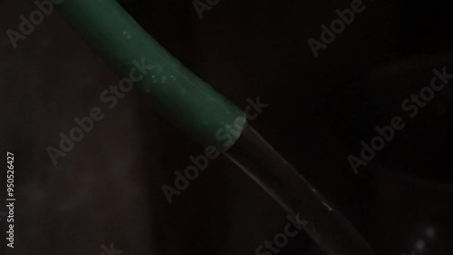 Green hose with water flowing out against a dark background.