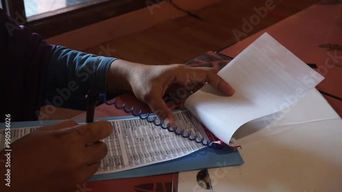 Person's hand writing on a spiral bound notebook.