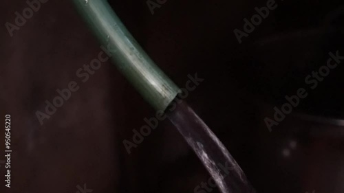 Water flowing from a green pipe against a dark background.