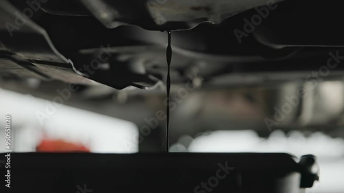 Old and wasted synthetic oil being drained into basin van beneath car and sprinter van garage floor as it pours out in slow motion and close-up into a bucket