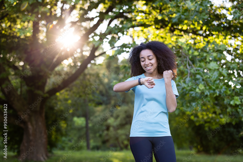 Joyful African American woman using phone fitness tracker outdoors, focusing on health and wellness. Sunlight filtering through trees creates uplifting atmosphere during exercise routine. Joyful African American woman using phone fitness tracker outdoors, focusing on health and wellness. Sunlight filtering through trees creates uplifting atmosphere during exercise routine.